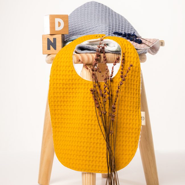 Baberos diferentes colores sobre un taburete de madera con flores secas de lavanda y las letras D y N en cubos de madera