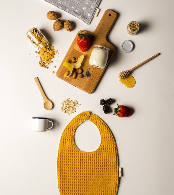 Babero de color mostaza con objetos y alimentos decorativos mostrando un desayuno saludable