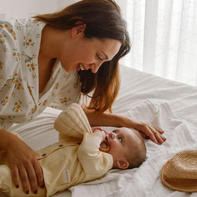 Bebé tumbado en la cama con su mamá con conjunto de dos piezas en color amarillo pastel